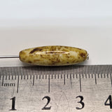 Close-up of a pile of brownish-golden cylindrical beads with dark spots on a ruler to show scale