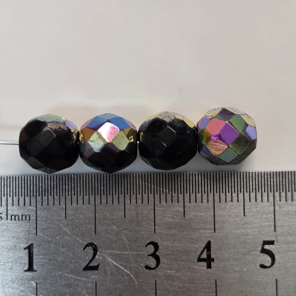 Four faceted beads with metallic iridescent finish on a ruler for scale.