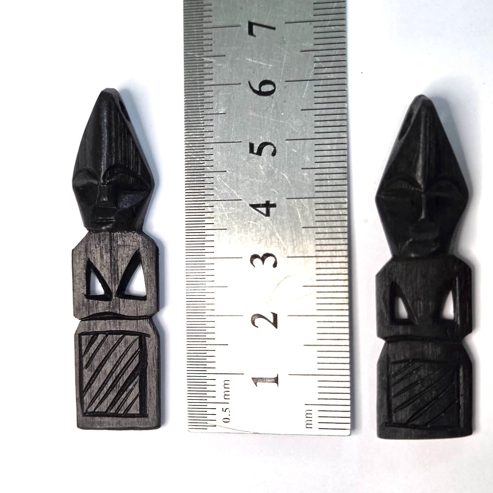 Two black wooden african folk art carvings on a white background with a ruler to show scale
