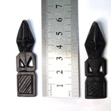 Two black wooden african folk art carvings on a white background with a ruler to show scale