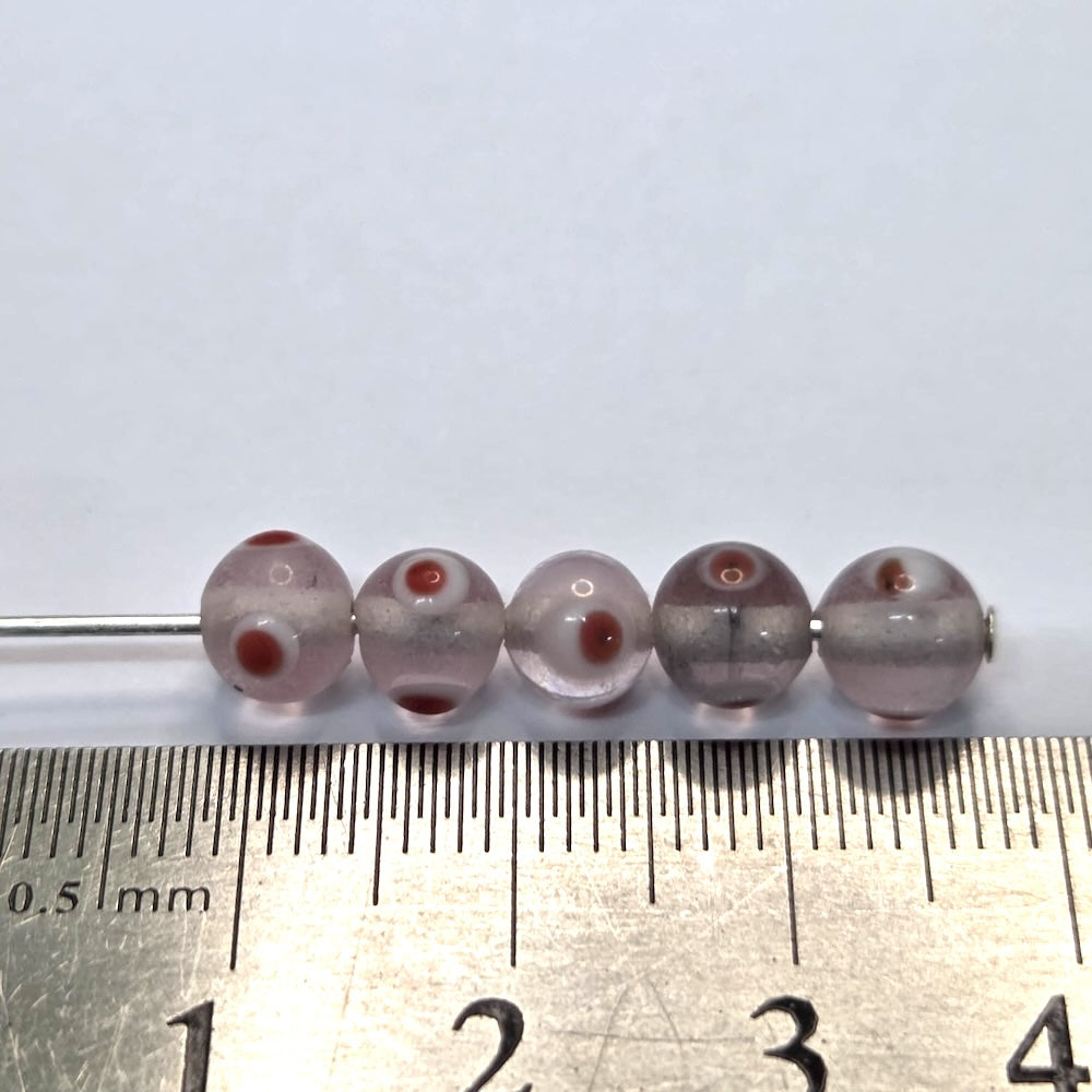 A collection of transparent clear glass beads with red and white eyes, used for making jewelry with a ruler for size