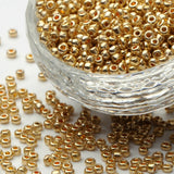 Gold glass seed beads in a clear glass bowl on a white background