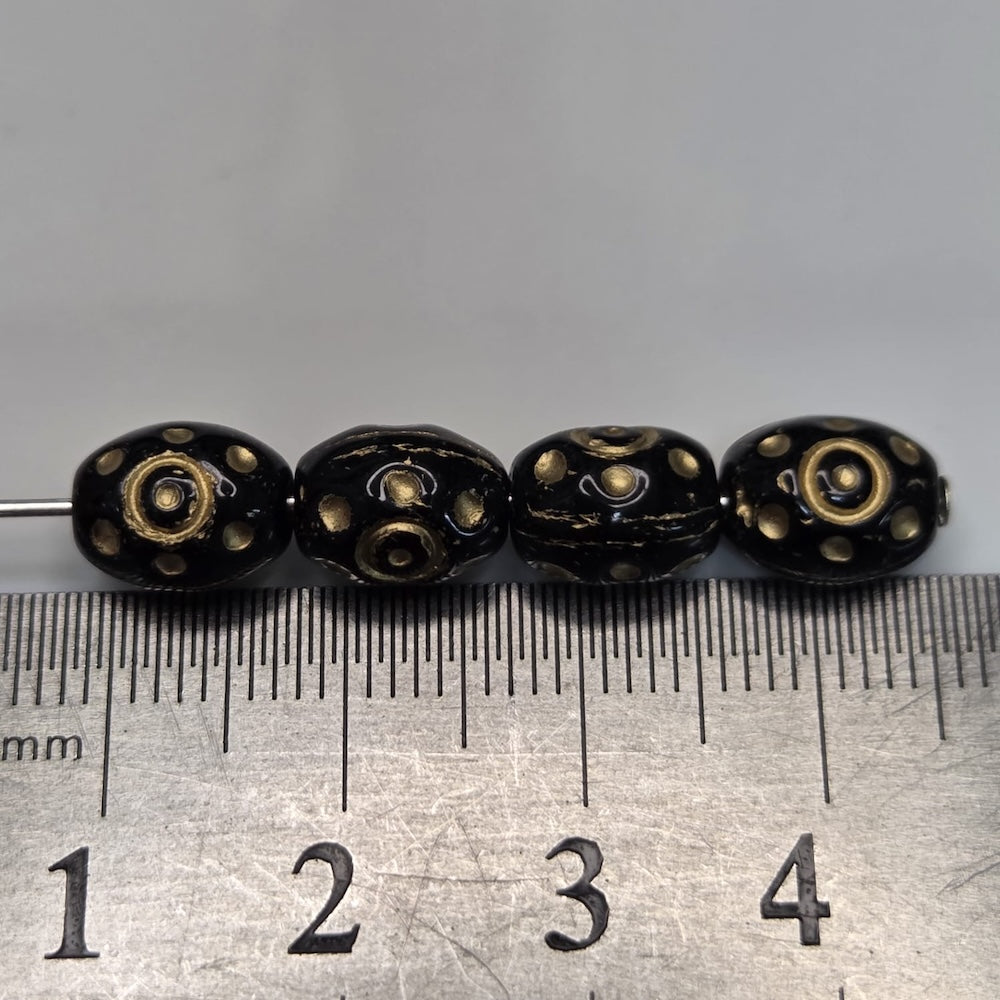 Four black beads with gold patterns on a ruler for size reference