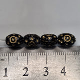 Four black beads with gold patterns on a ruler for size reference