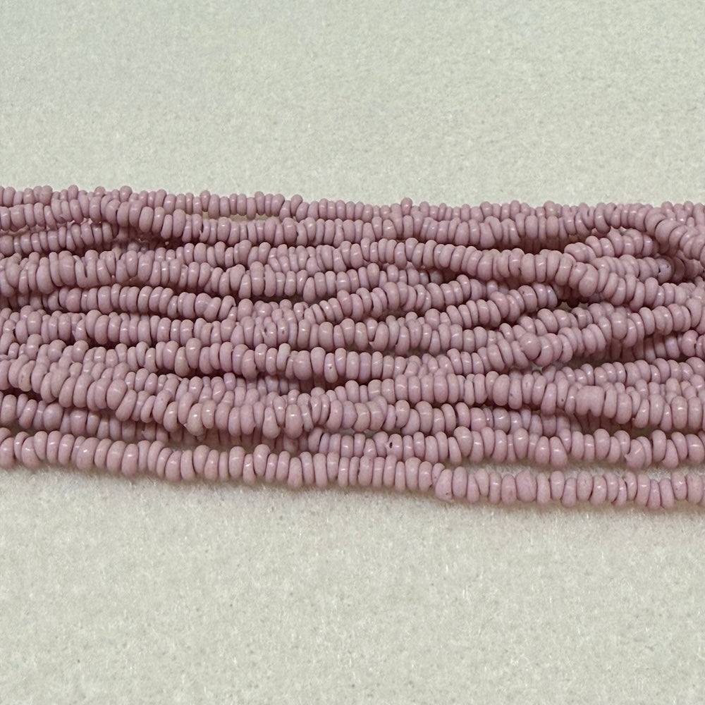 dusty pink color mini glass donut beads on strands on a cream background