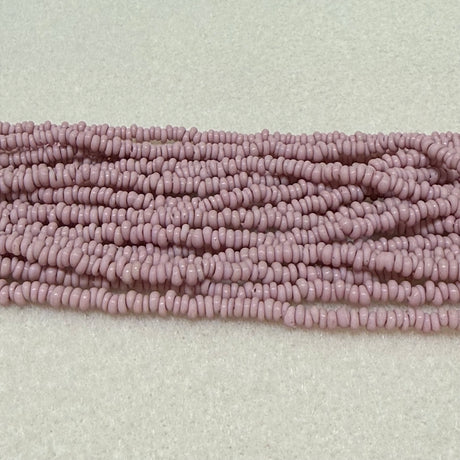 dusty pink color mini glass donut beads on strands on a cream background