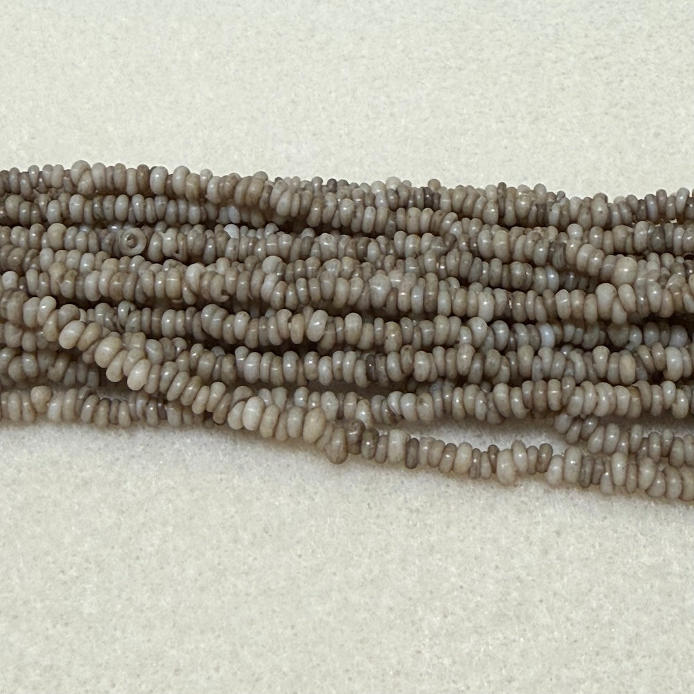 stone color mini glass donut beads on strands on a cream background