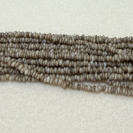 stone color mini glass donut beads on strands on a cream background