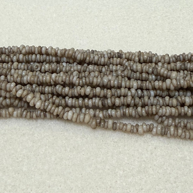 stone color mini glass donut beads on strands on a cream background