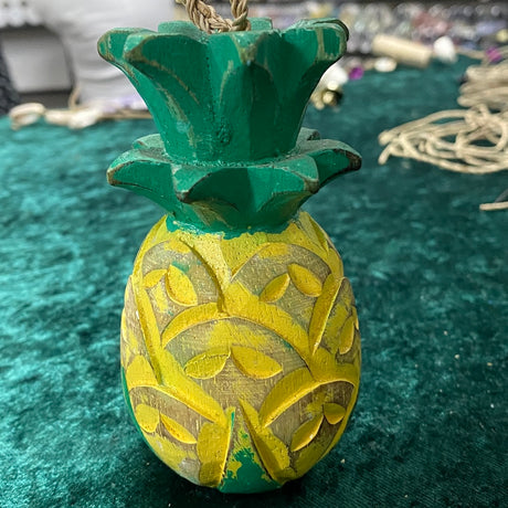 A hand painted and hand carved wooden decoration resembling a pineapple with yellow and green colors, intended for nautical themed decorations.