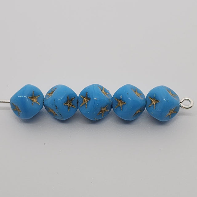 A collection of light blue cube-shaped beads with gold stars etched on them threaded on a pin