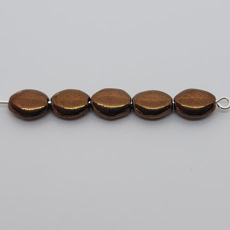 lustrous bronze oval flat beads on a pin on a grey surface