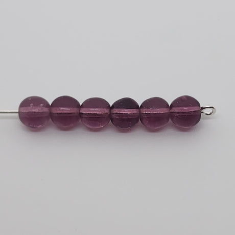 round purple glass beads on a pin on a grey background