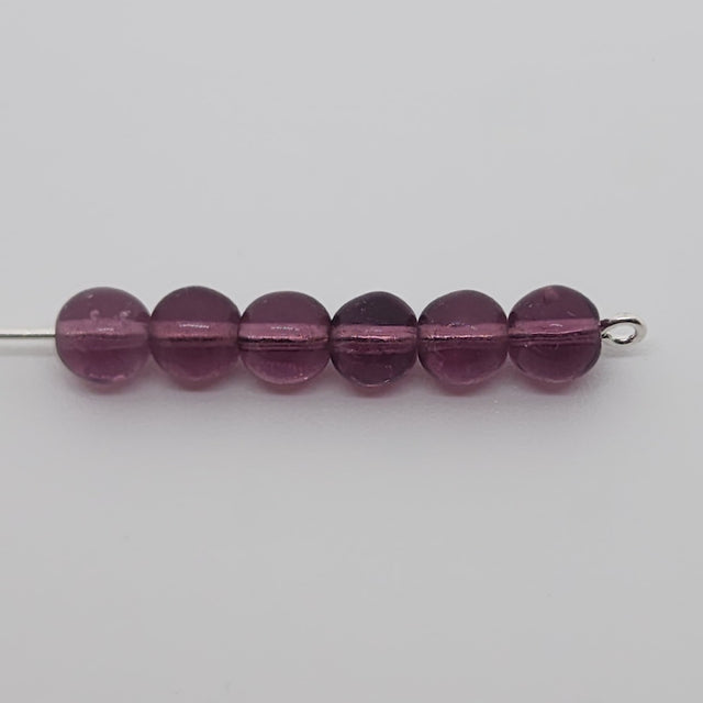 round purple glass beads on a pin on a grey background