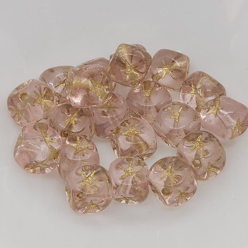 A collection of pink cube-shaped beads with gold etched stars on them.