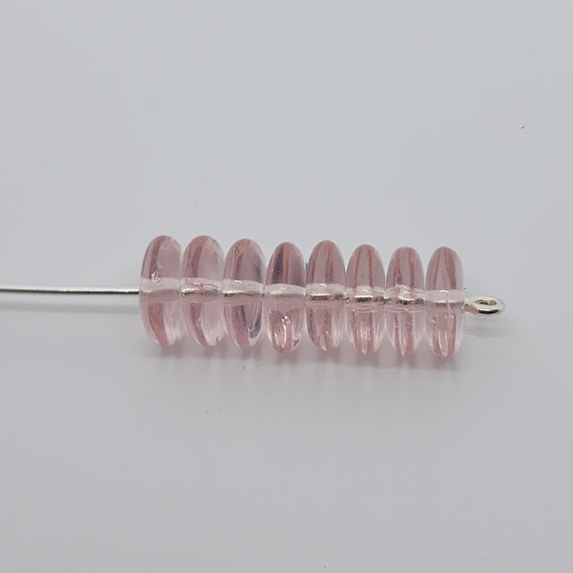 pale pink flat beads threaded on a pin to show the direction of the hole, on a grey surface