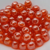 A collection of orange round Czech glass beads on a white surface.