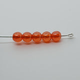 A collection of orange round Czech glass beads on a white surface threaded on a pin