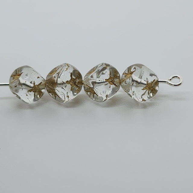 A collection of clear cube-shaped beads with gold etched stars, intended for use in jewelry making threaded on a pin to show the clear shape